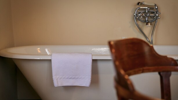A bathroom with a bathtub, a white towel, and a wooden chair. - J And J Historic House Hotel (Florence)