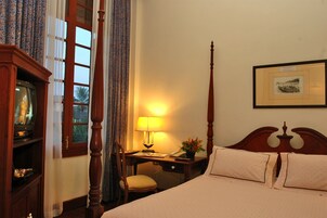Una camera d'albergo con un letto, una scrivania con una lampada, una sedia, una televisione e tende.
