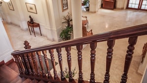 A grand staircase with a wooden handrail leading to a spacious lobby area with a high ceiling, columns, and a large window. - Settha Palace Hotel (Vientiane)