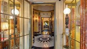 A grand hallway with a marble floor, ornate lamps, and a glass partition. - L'Hotel (Paris)