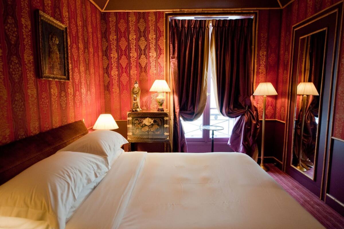 A hotel room with a large bed, two bedside lamps, a small table with a decorative item, and a mirror.