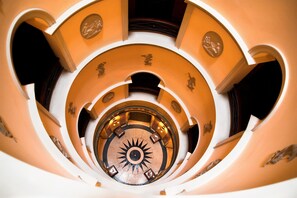 A spiral staircase with a central sun-like design, surrounded by ornate wall decorations and a circular floor pattern. - L'Hotel (Paris)