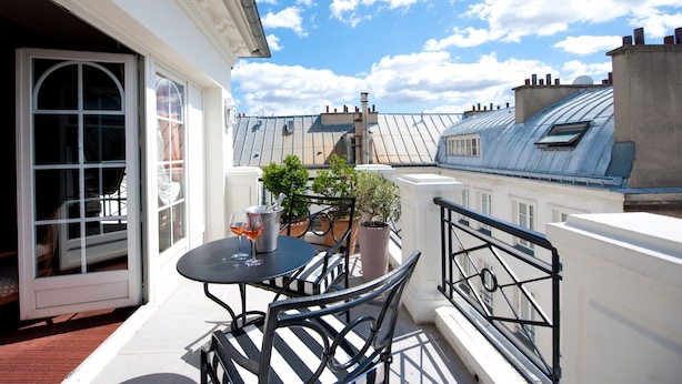 A balcony with a table, chairs, potted plants, and a view of the cityscape. - L'Hotel (Paris)