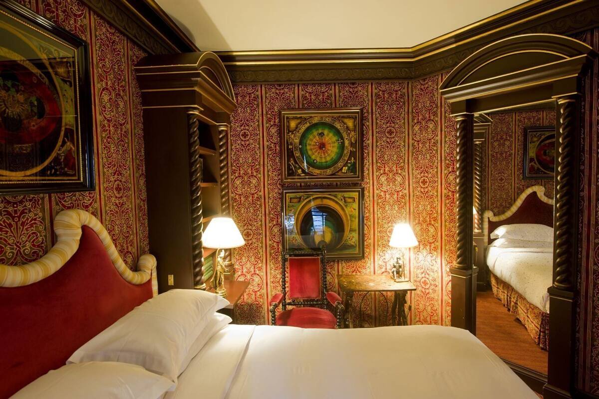 A hotel room with a large bed, two bedside tables, a chair, and ornate wallpaper.