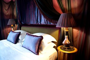 A bed with white linens and purple pillows, a dark-colored headboard, and two bedside lamps on wooden side tables. - L'Hotel (Paris)