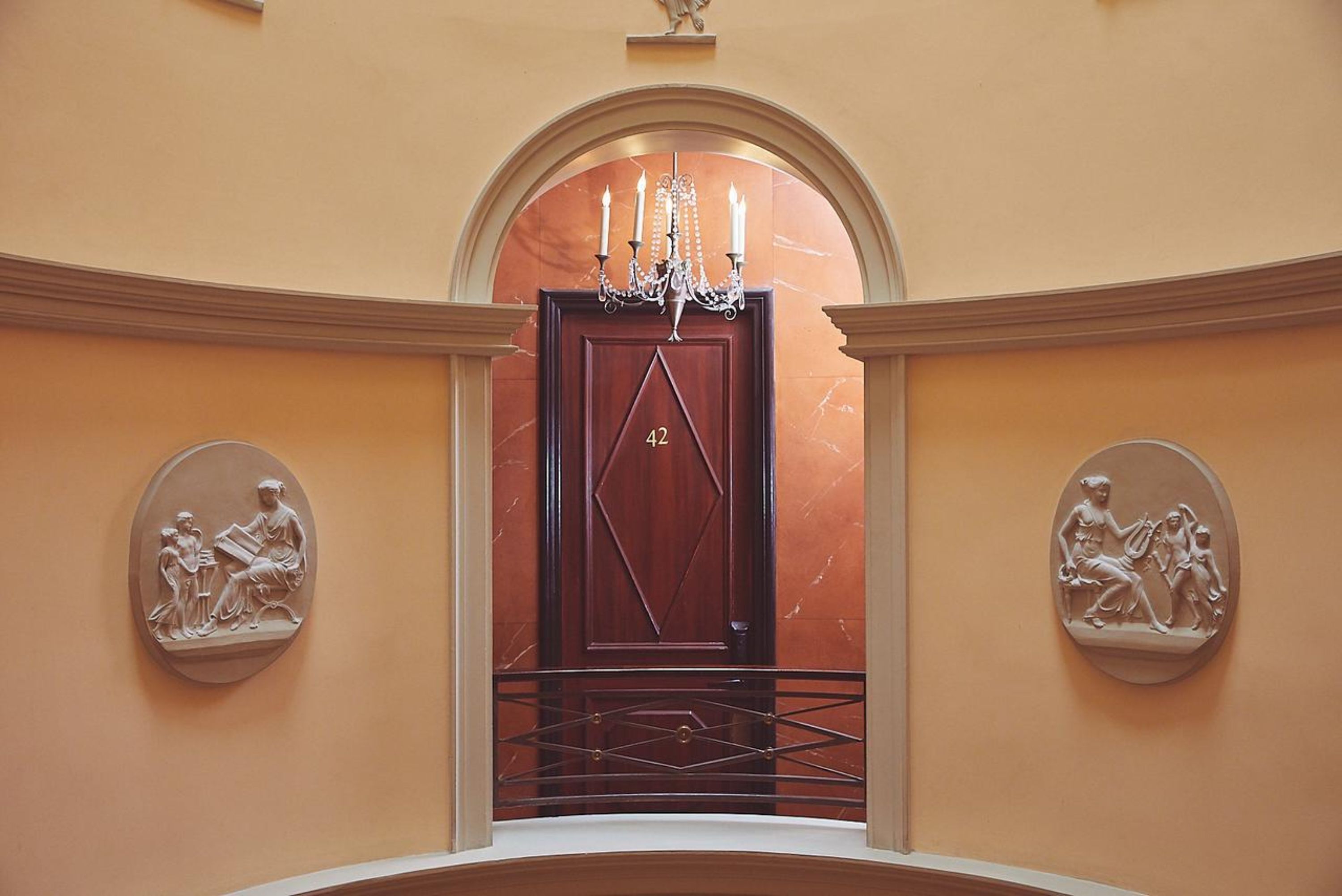 Une entrée somptueuse, avec une porte en marbre, un lustre et des sculptures en relief de style classique sur les murs.