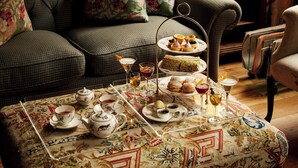 Una sala de estar acogedora con un juego de té de tres niveles sobre una mesa estampada, un sofá y una estantería al fondo.