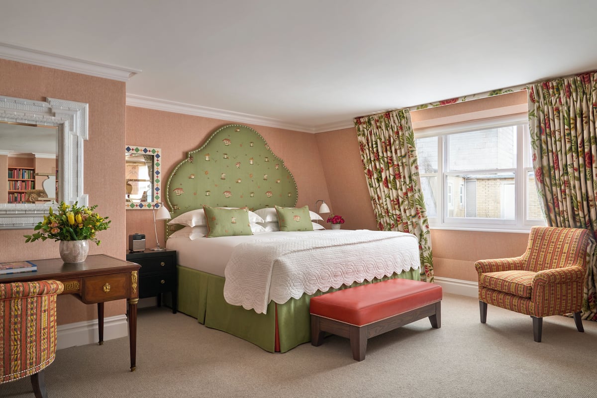 A bedroom with a bed, a desk, a chair, a window with curtains, and a mirror.