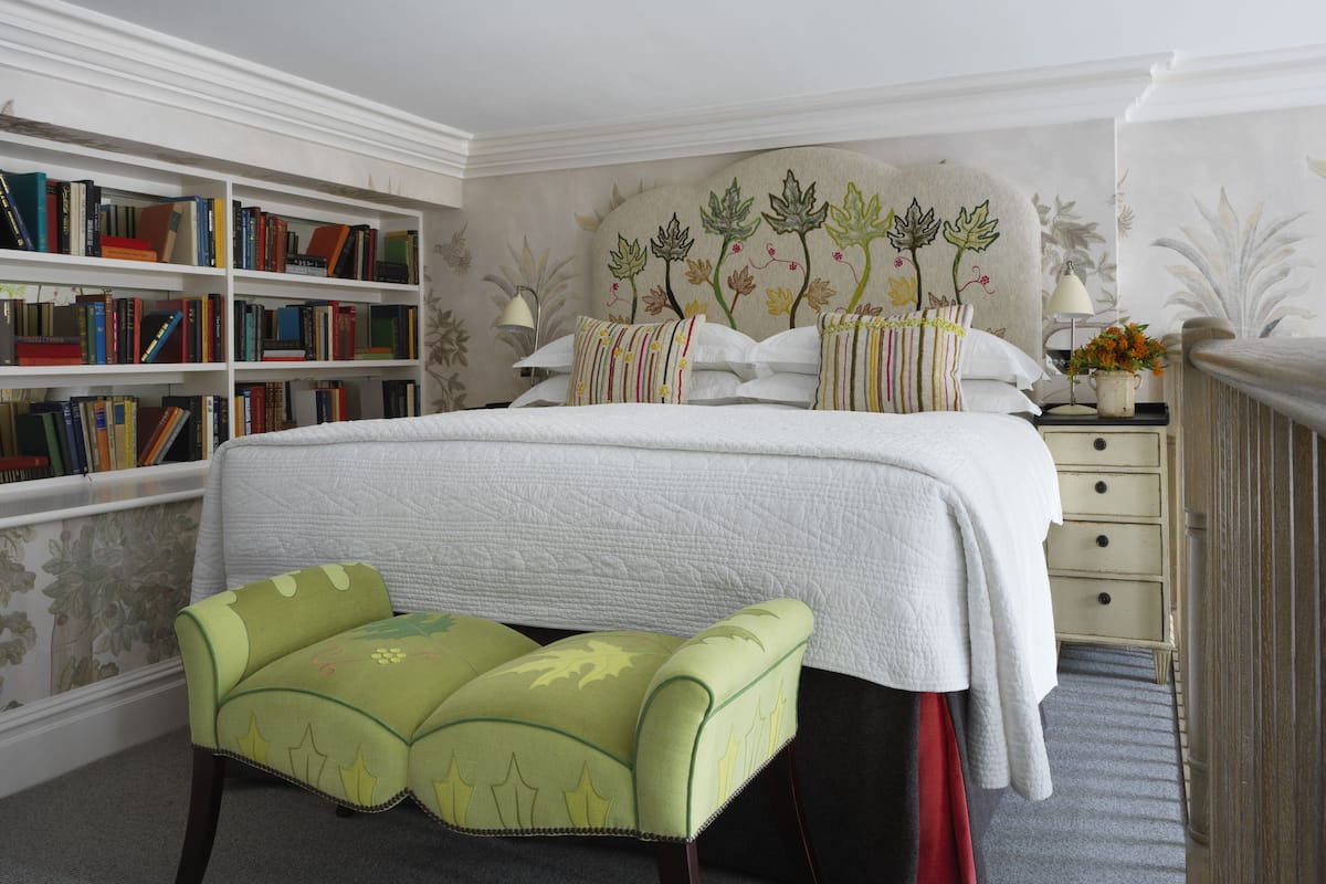 A bedroom with a large bed, a bookshelf, a nightstand, and a green upholstered bench.