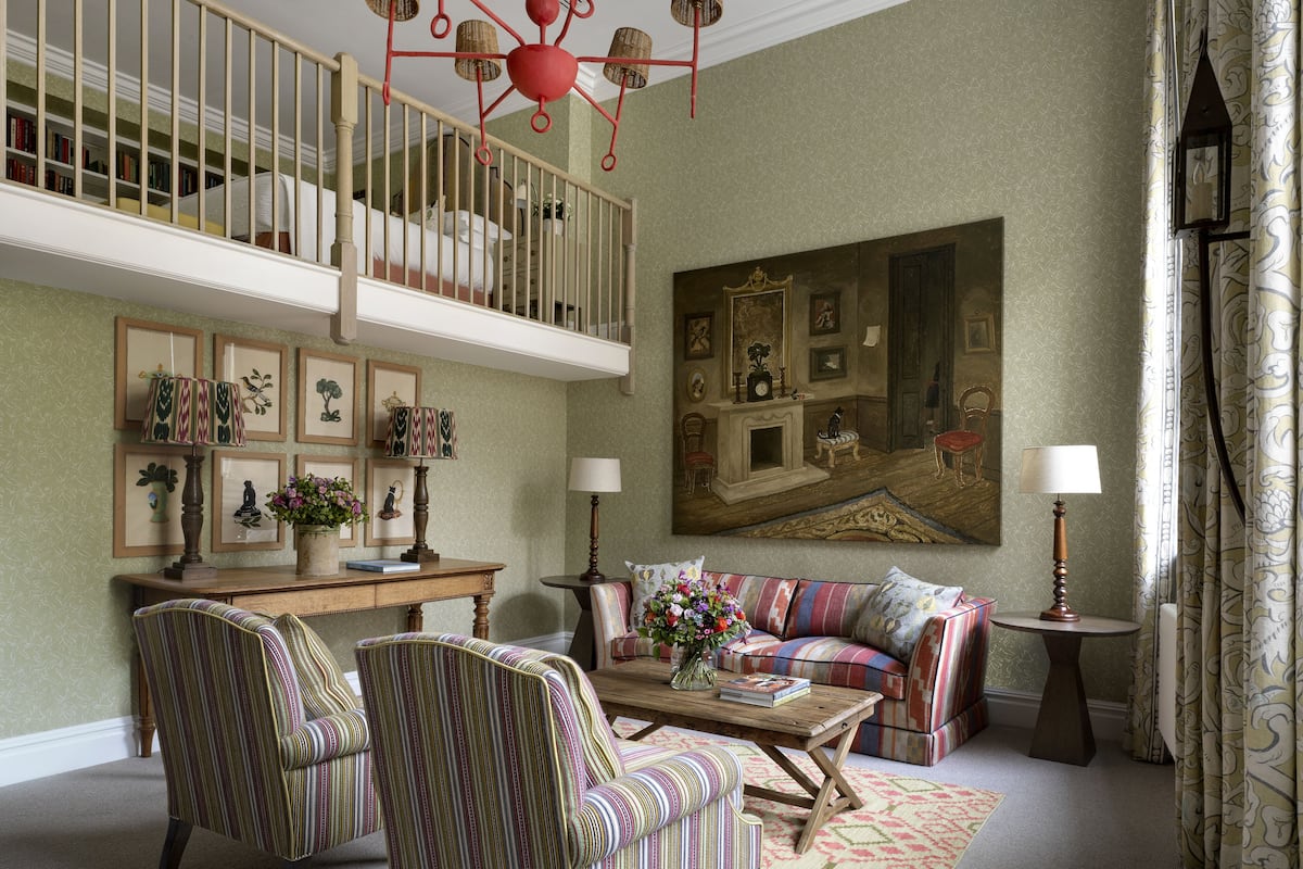 A spacious living room with a high ceiling, a staircase, a large painting, and a cozy seating area.