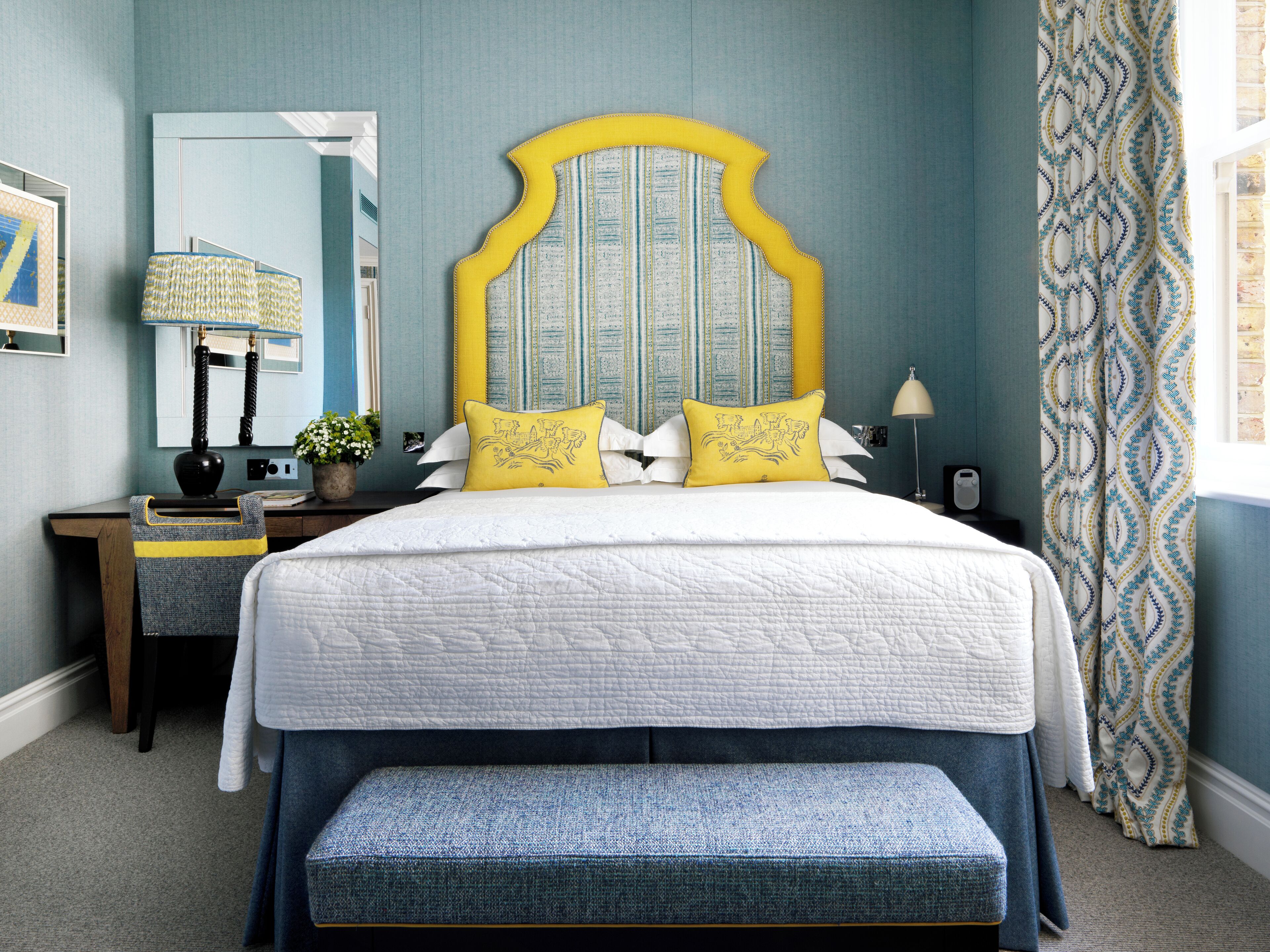 A neatly arranged bedroom with a large bed, bedside tables, a lamp, and a bench.