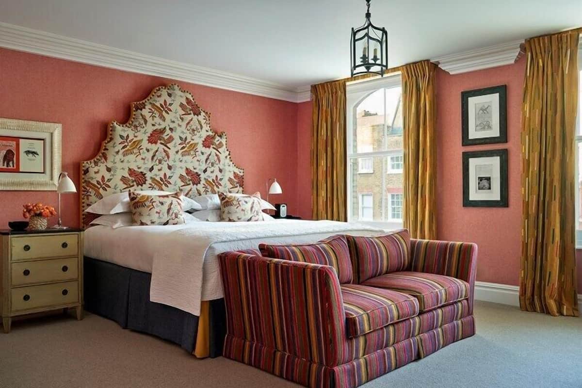 A bedroom with a large bed, a striped sofa, a nightstand, and a window with curtains.