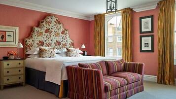 A bedroom with a large bed, a striped sofa, a nightstand, and a window with curtains.