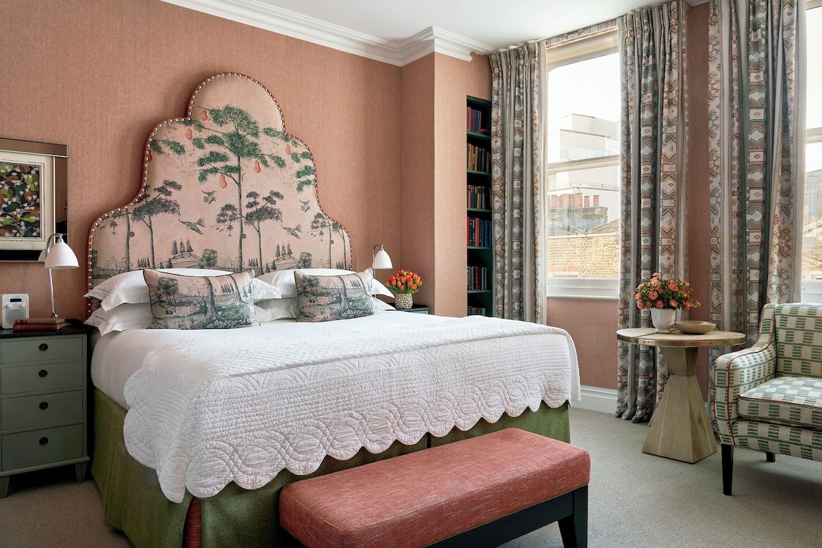 A bedroom with a large bed, a bench, a chair, a small table, and a bookshelf.