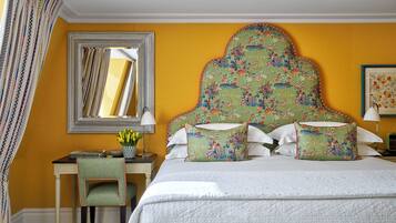 A hotel room with a large bed, a desk with a chair, a mirror, and a floral-patterned headboard.