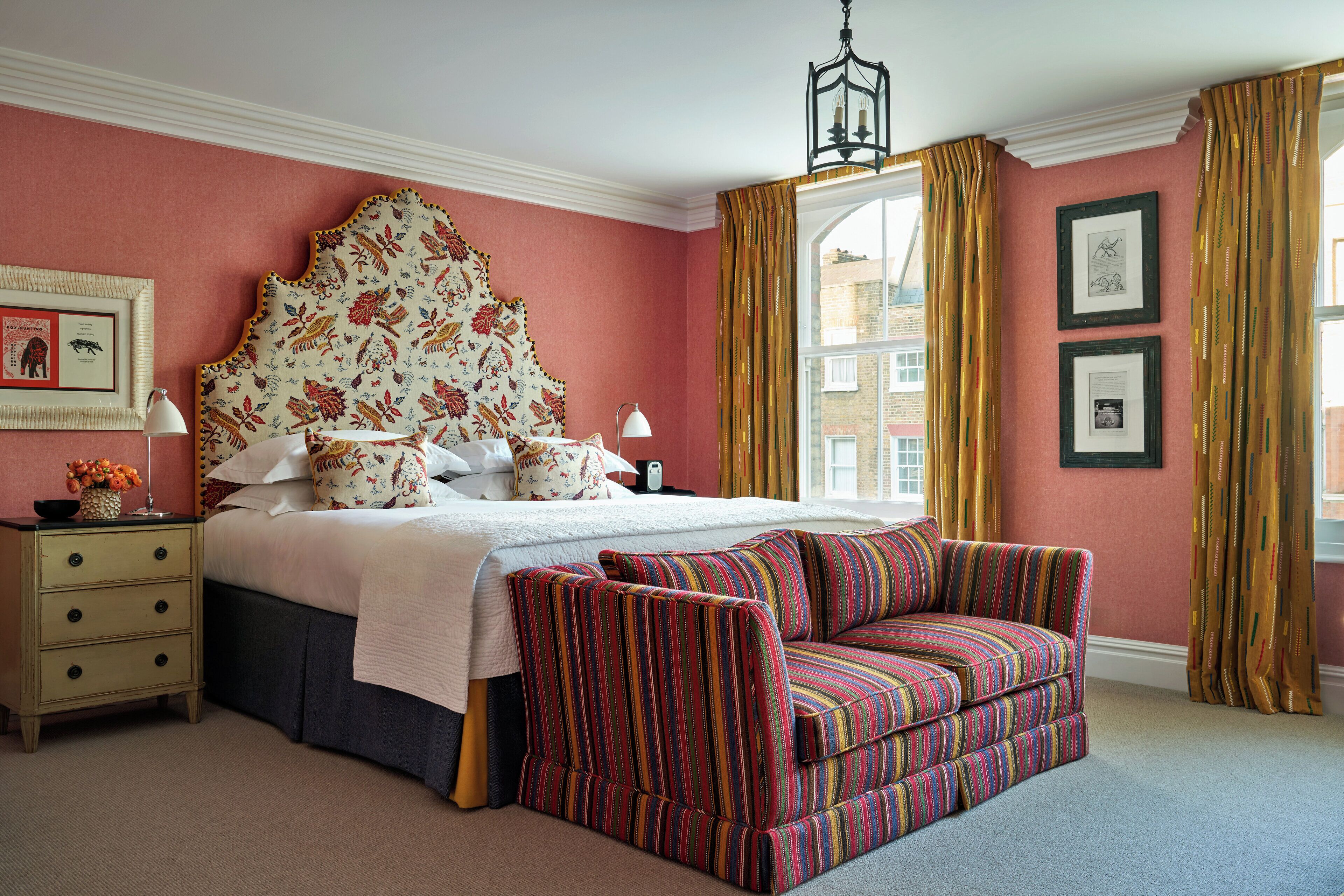 A bedroom with a large bed, a nightstand, a lamp, a sofa, and a window with curtains.