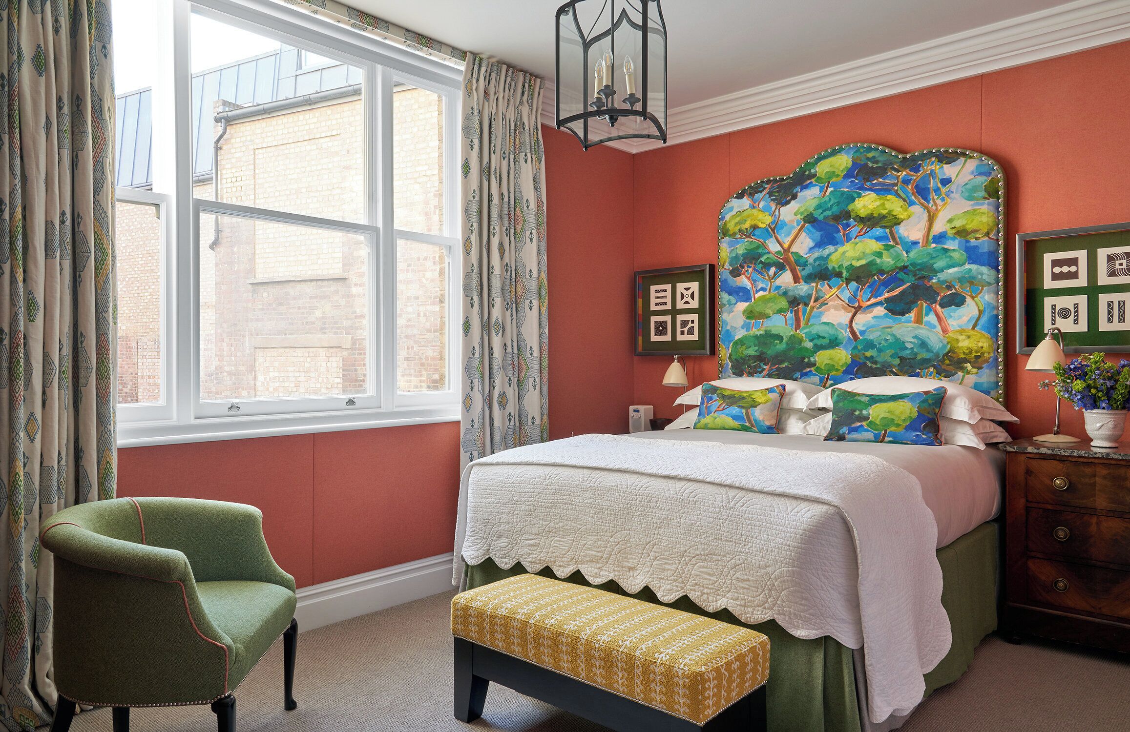 A bedroom with a large bed, a green armchair, a bench, and a window with curtains.