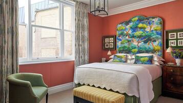 A bedroom with a large bed, a green armchair, a bench, and a window with curtains.