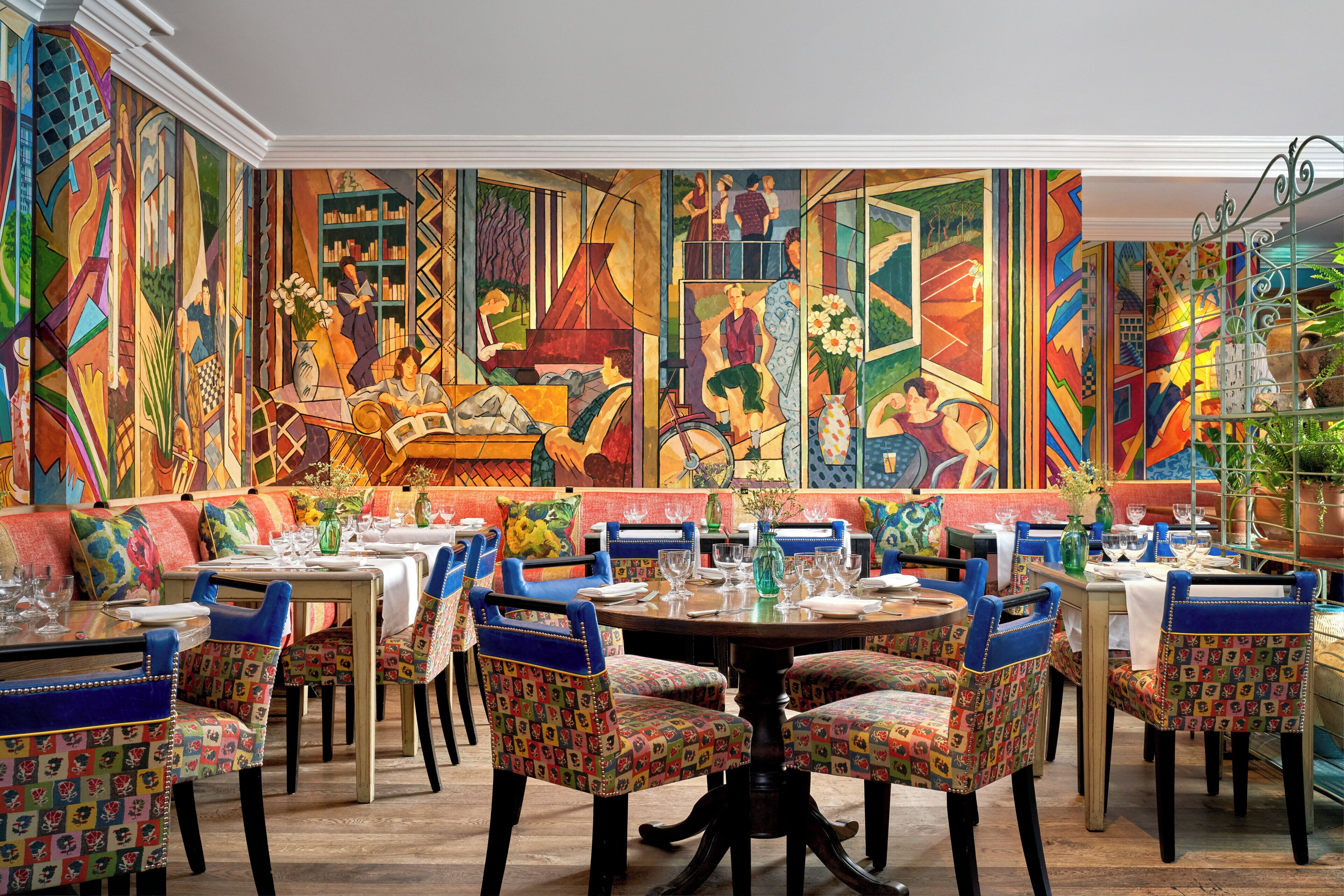 A dining area with colorful chairs, tables, and a mural on the wall.