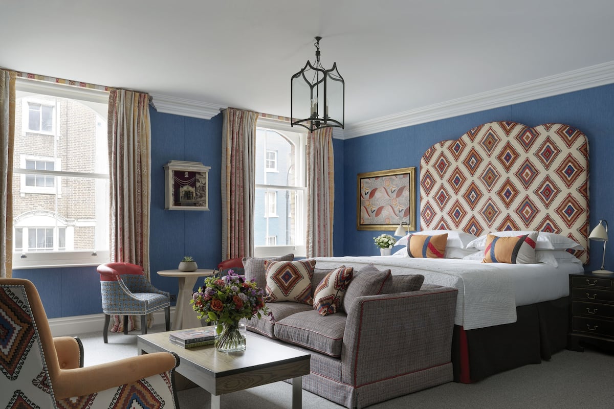 A bedroom with a bed, a sofa, a chair, a table, and a window with curtains.
