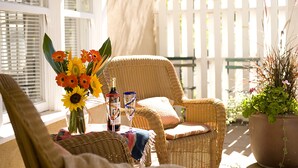 A wicker chair and table with a vase of flowers, a bottle, and glasses. - Las Palomas (Santa Fe)