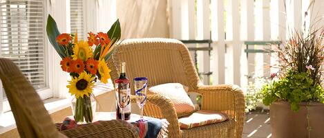 A wicker chair and table with a vase of flowers, a bottle, and glasses.
