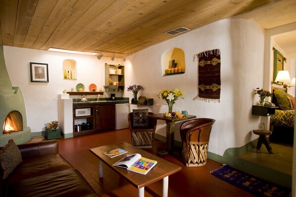 A cozy living room with a fireplace, wooden furniture, and a kitchen area with shelves and a microwave.