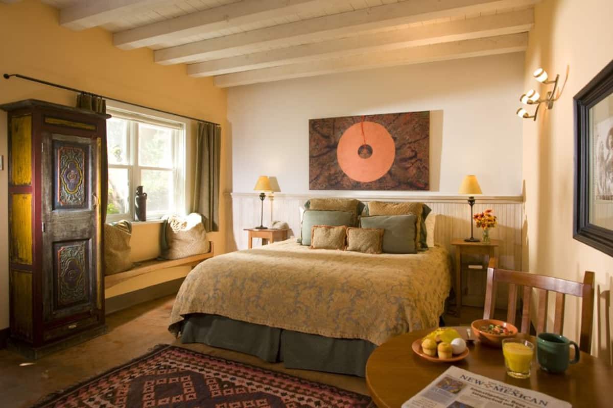 A cozy bedroom with a large bed, a window with curtains, a bedside table with lamps, and a breakfast setup on the side.
