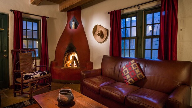 A cozy room with a fireplace, leather sofa, wooden table, and a chair. - Las Palomas (Santa Fe)