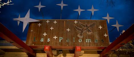 A wooden sign with the text "Las Palmas" and a dove symbol, mounted on a structure with red supports.