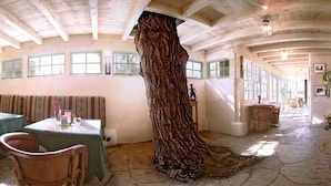 A restaurant with a unique tree trunk centerpiece, stone flooring, and a high ceiling with exposed beams. - Las Palomas (Santa Fe)