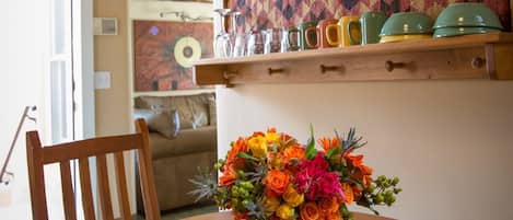 Una mesa de comedor con un florero, una silla de madera y una estantería con vajilla y copas.