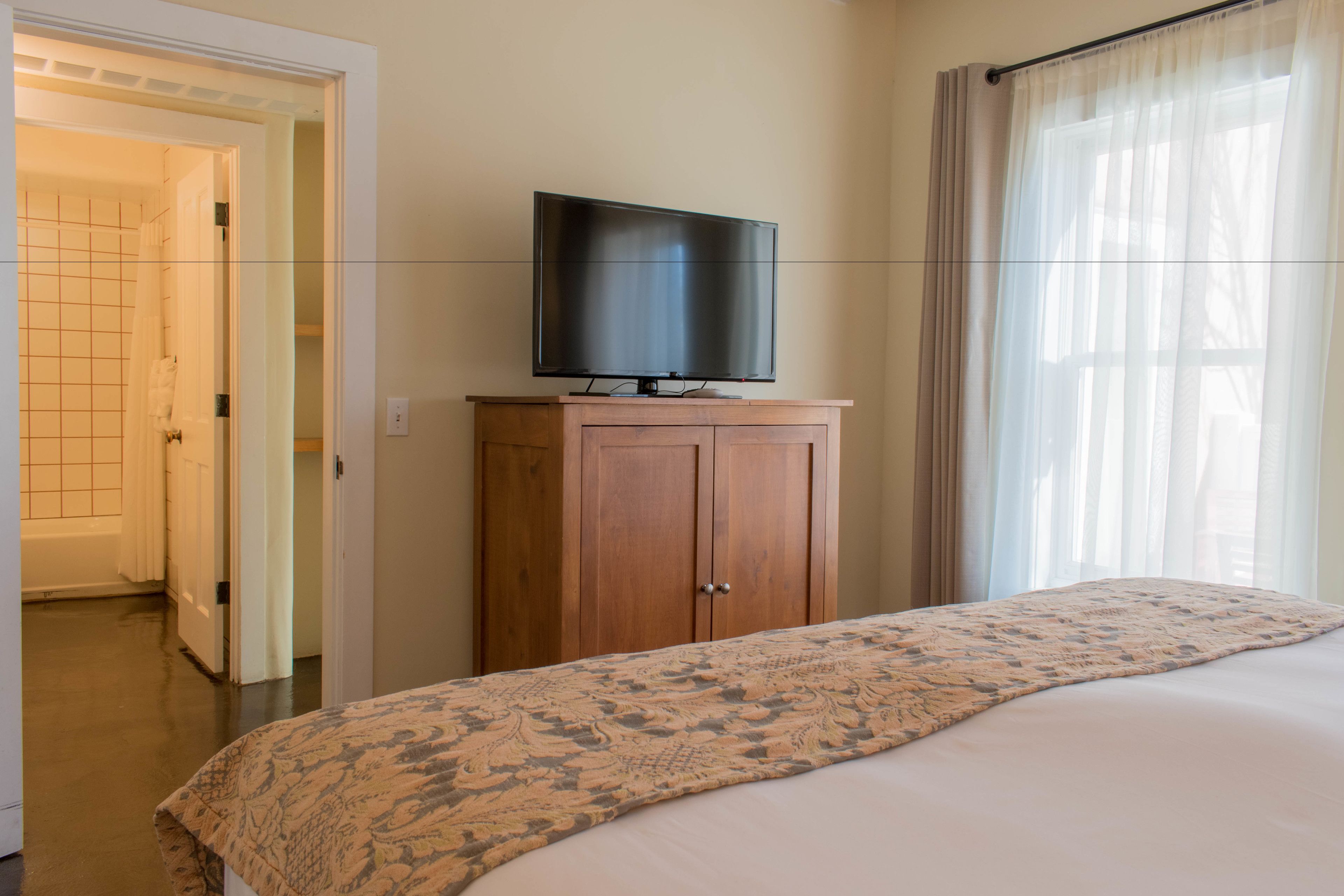 A hotel room with a bed, a television on a wooden cabinet, and a bathroom visible through an open door.