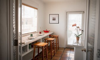 A kitchen with a tiled backsplash, a window with blinds, a red pot on the counter, and a potted orchid by the door.