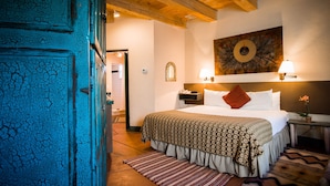 A hotel room with a bed, a nightstand, a lamp, a mirror, and a door. - Las Palomas (Santa Fe)