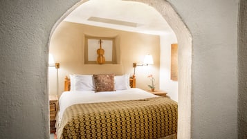 A bedroom with a bed, pillows, a lamp, a guitar, and a small table with a plant.