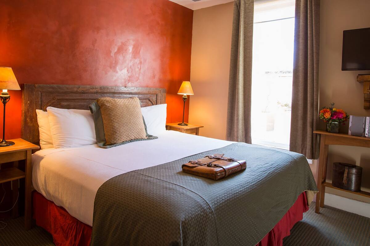 A hotel room with a large bed, two bedside lamps, a television, and a small table with a vase of flowers.