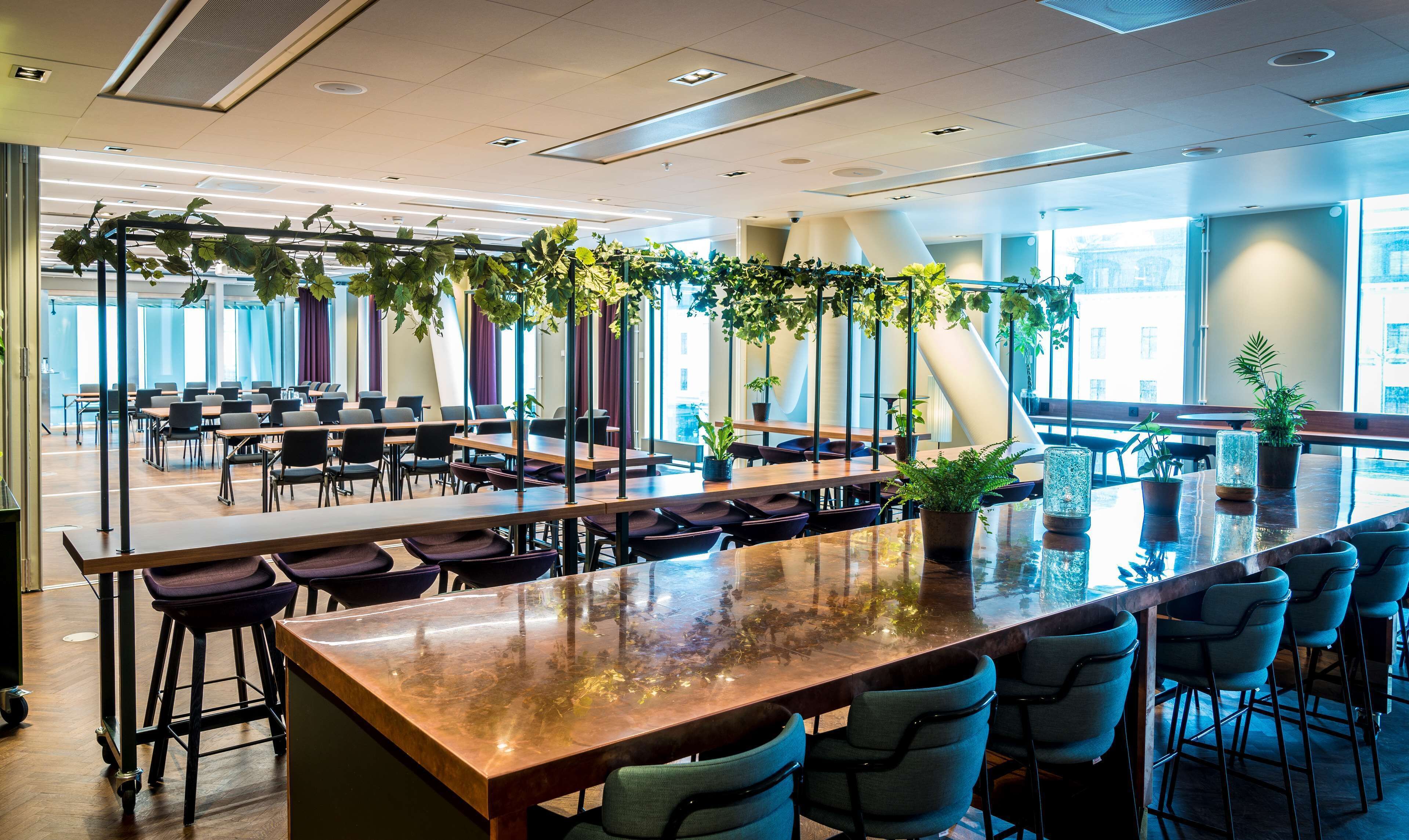 A spacious indoor area with multiple tables and chairs, large windows, and indoor plants.