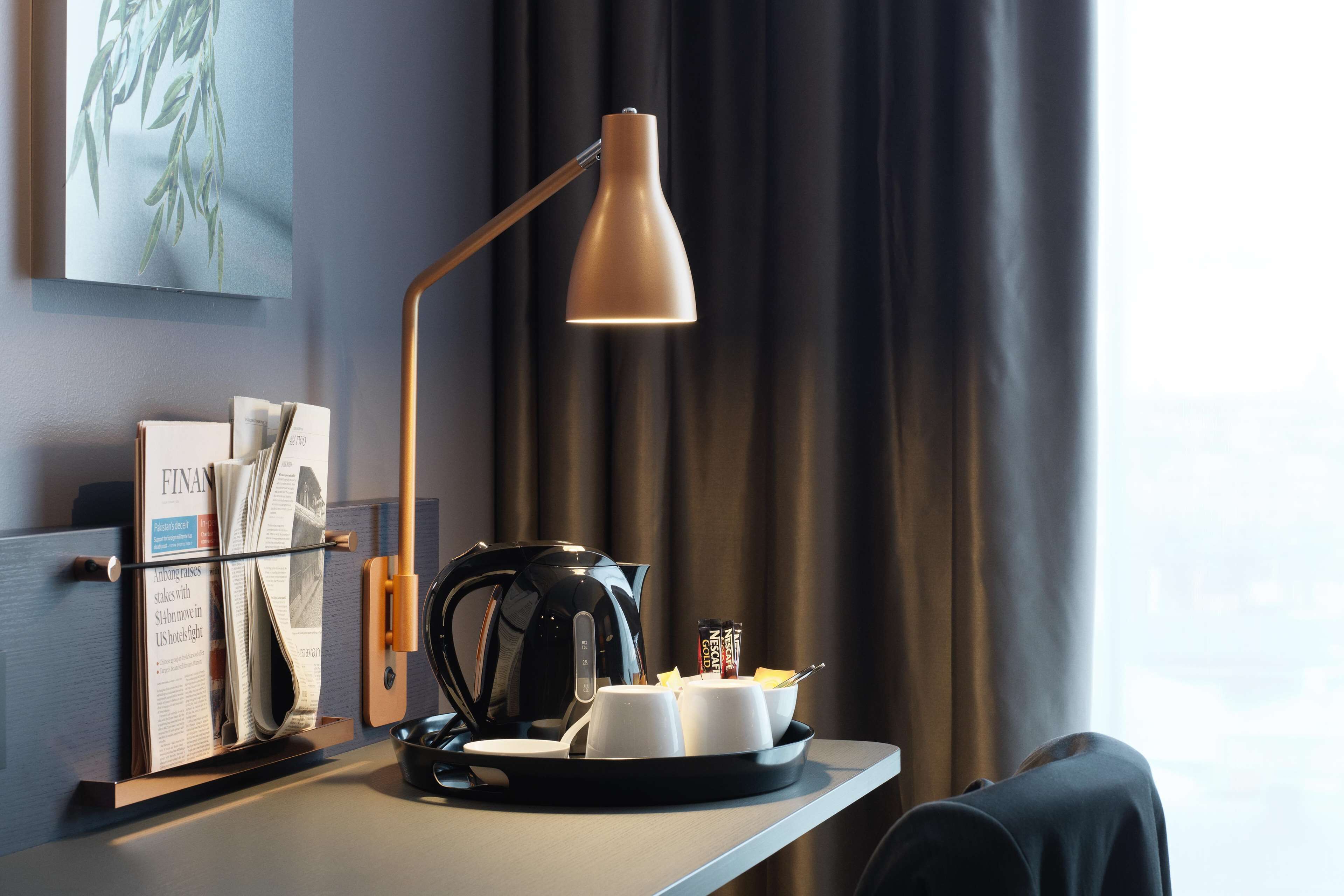 Hotellihuone, jossa on työpöytä, kahvinkeitin, kuppeja, tarjotinalusta ja lehtiteline.