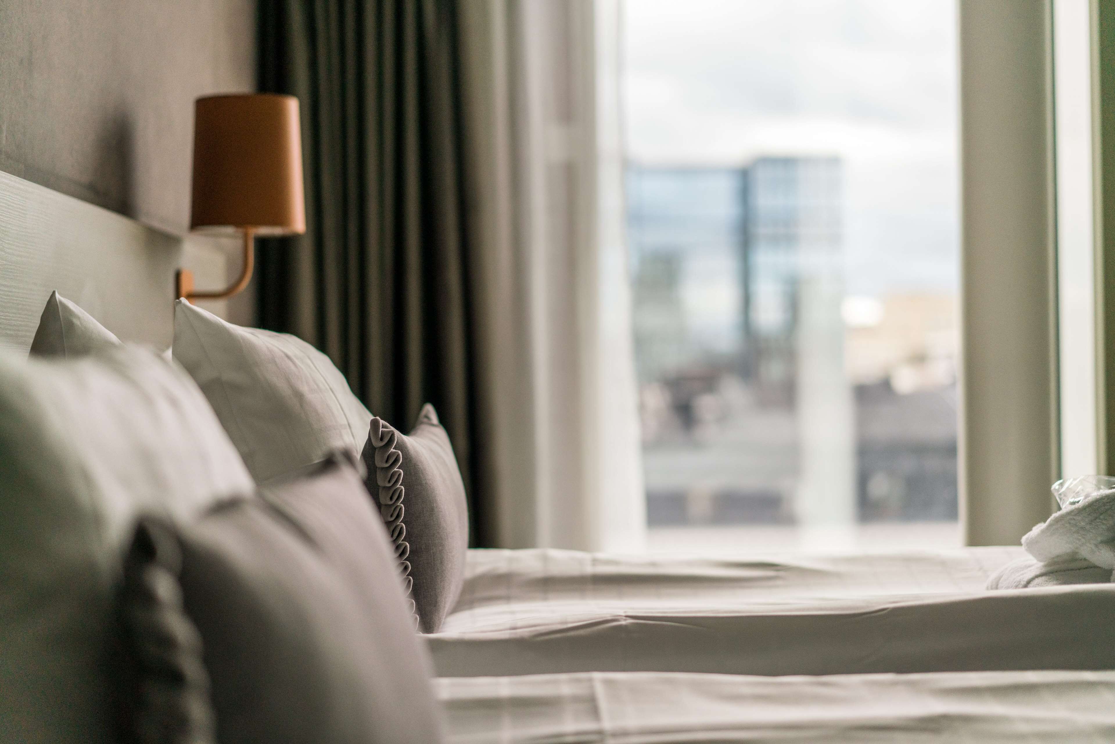 A hotel room with a bed, a lamp, and a view of a cityscape through the window.