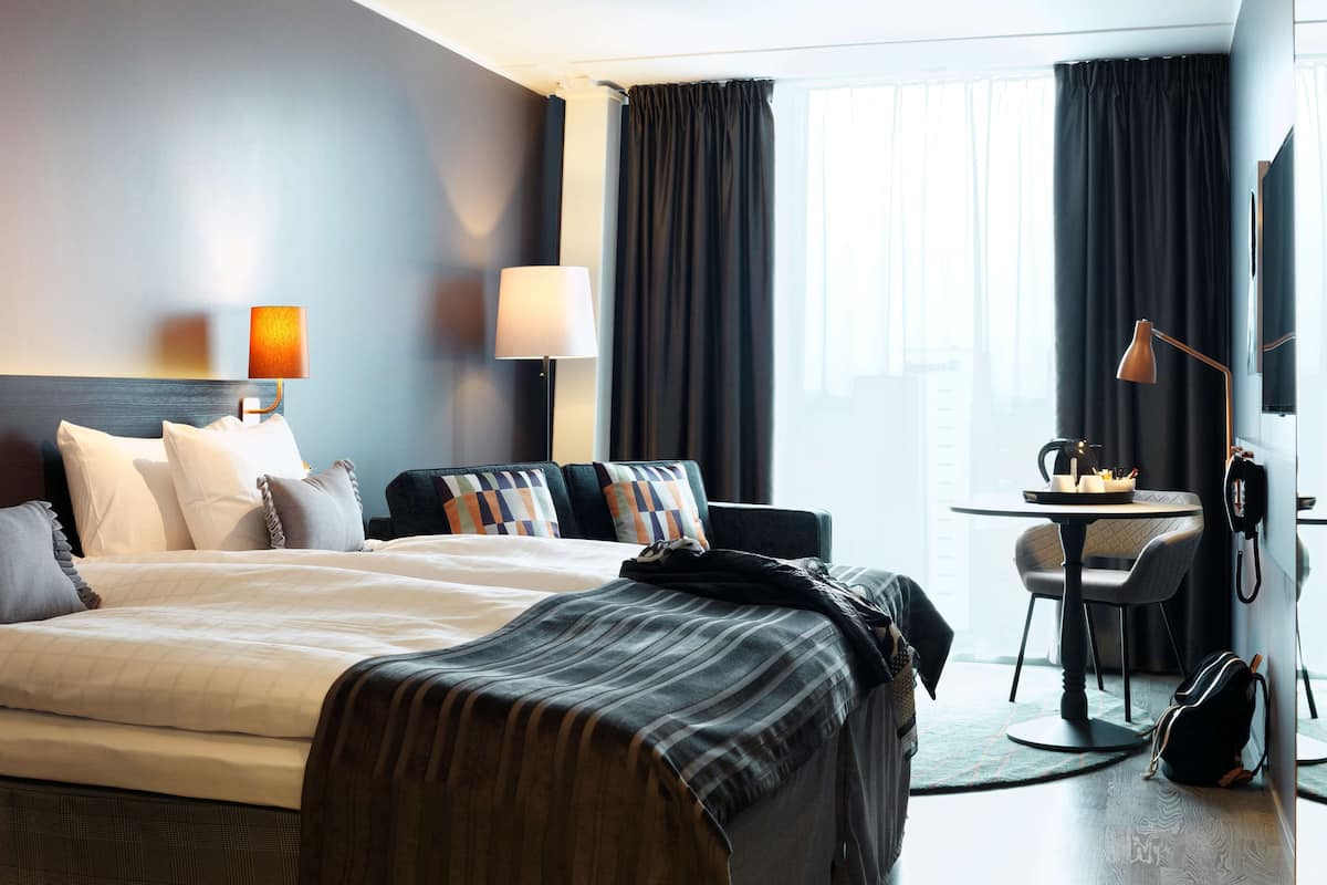 A hotel room with a bed, a desk, a chair, a lamp, and a TV.