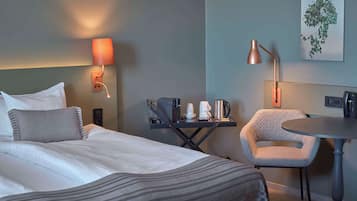 Habitación de hotel con cama, mesita de noche, silla y lámpara de pared.
