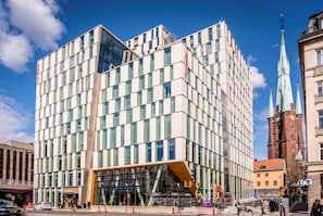 A modern hotel with a glass facade, a prominent entrance, and a clock tower in the background.