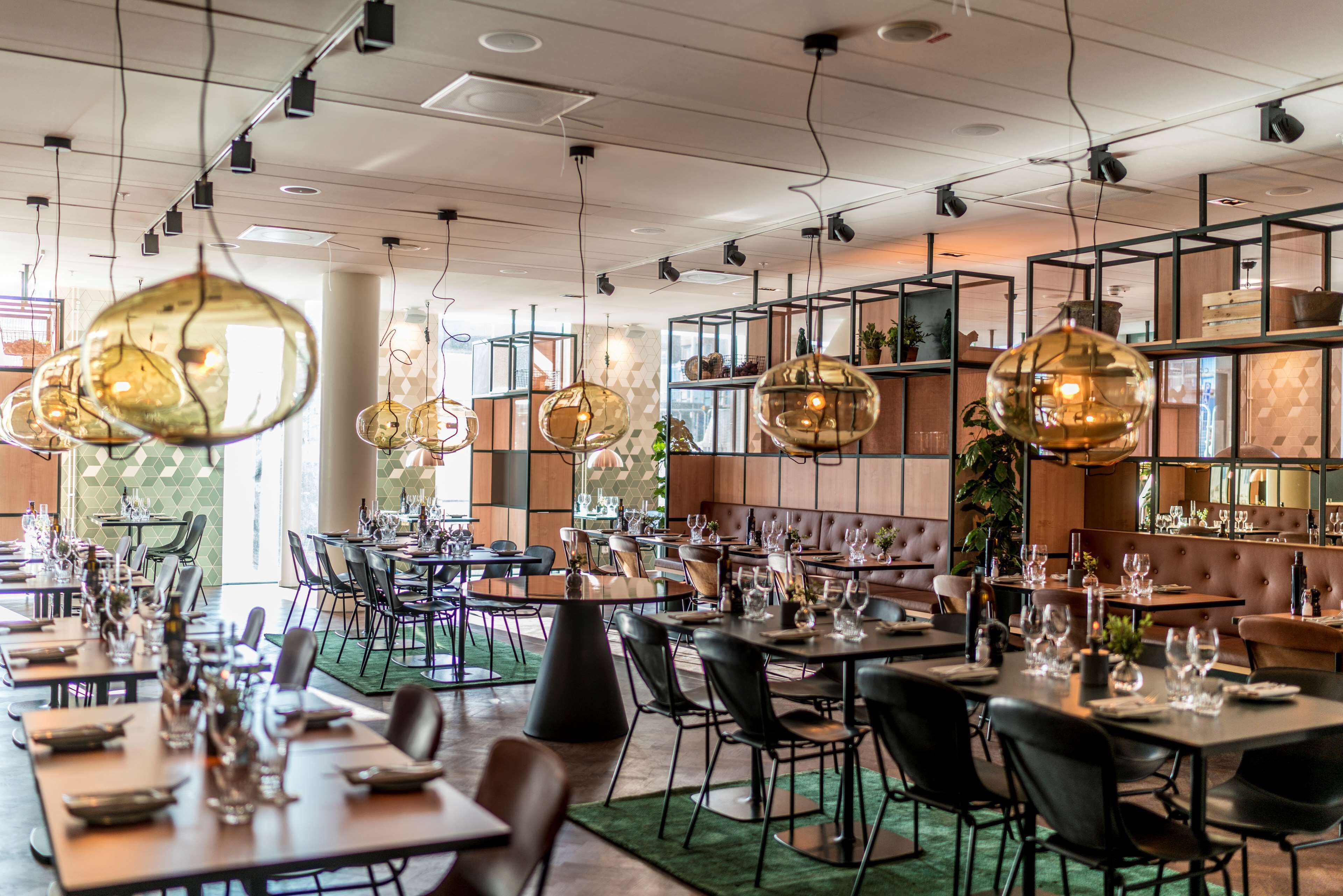 Een restaurant met meerdere eettafels, stoelen, hangende lampen en planken met planten.