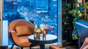 A modern interior with a leather chair, a round table, and a view of a busy city street through large windows. - Scandic Continental (Stockholm)