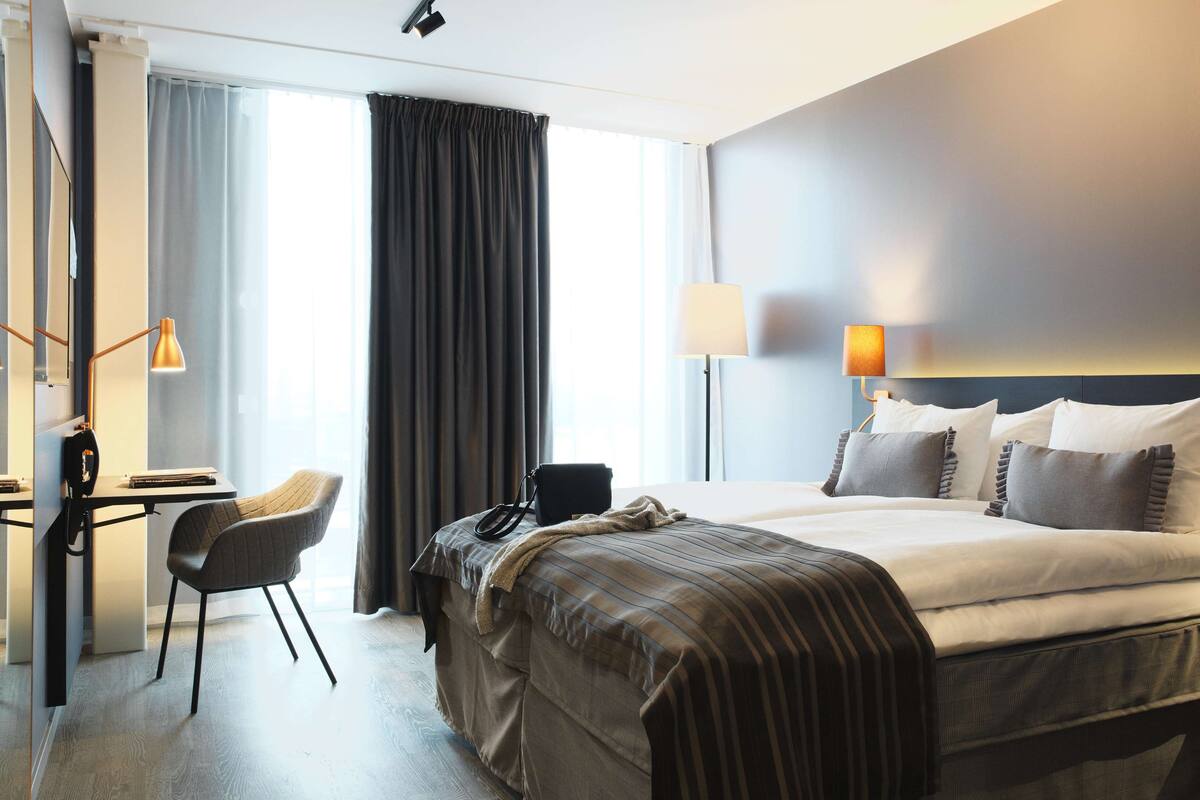 A hotel room with a bed, desk, chair, and lamps.