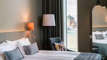 Quarto de hotel com uma cama grande, uma cadeira, um abajur, um espelho e vista para um edifício.