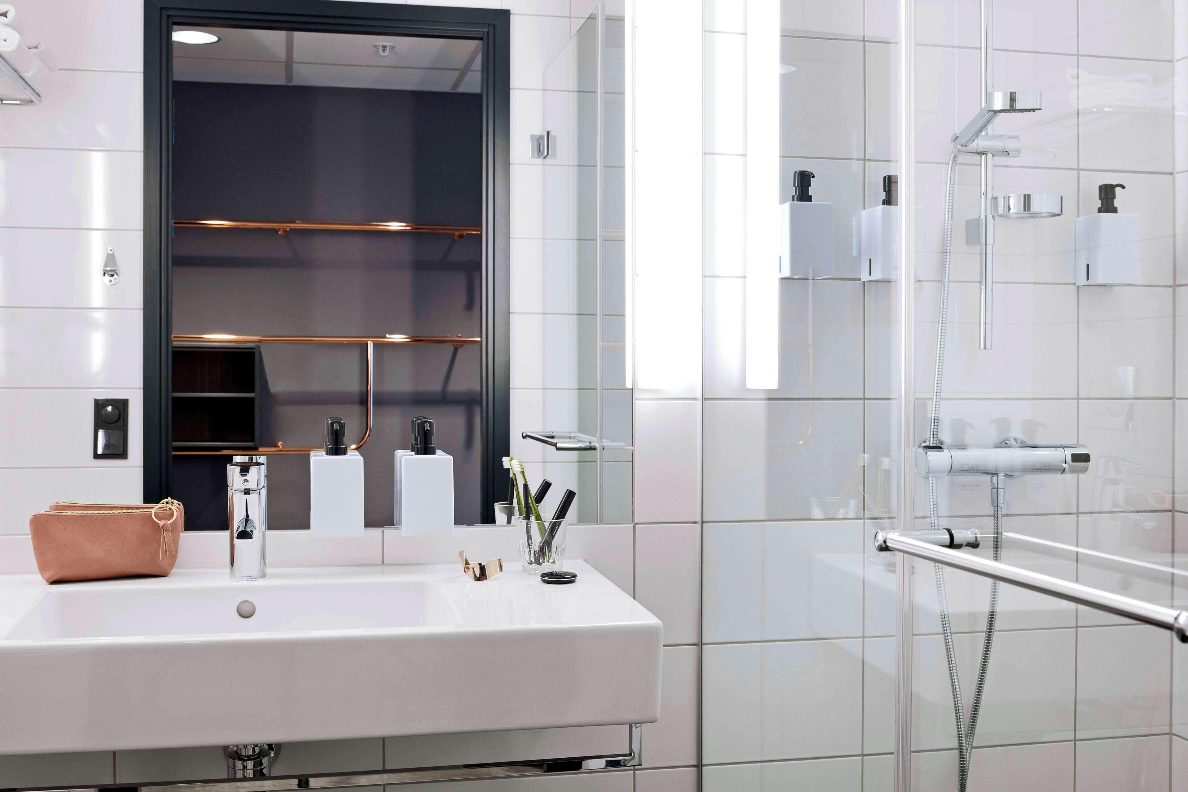 Un baño moderno con un espejo grande, un lavamanos blanco y una zona de ducha con mampara de vidrio.