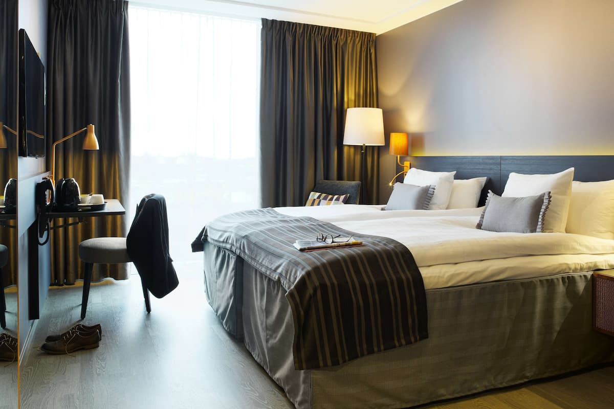 A hotel room with a large bed, a desk with a lamp, a chair, and a view of the outdoors.