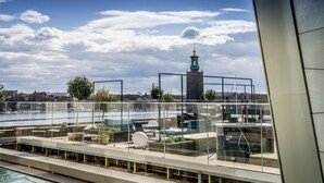 A rooftop terrace with outdoor seating, a view of a river, and a distant tower. - Scandic Continental (Stockholm)